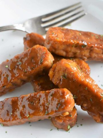 cooked tempeh strips on a white plate with a fork on it