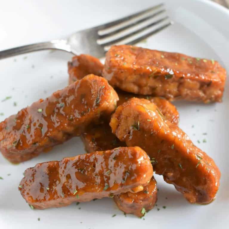 cooked tempeh strips on a white plate with a fork on it