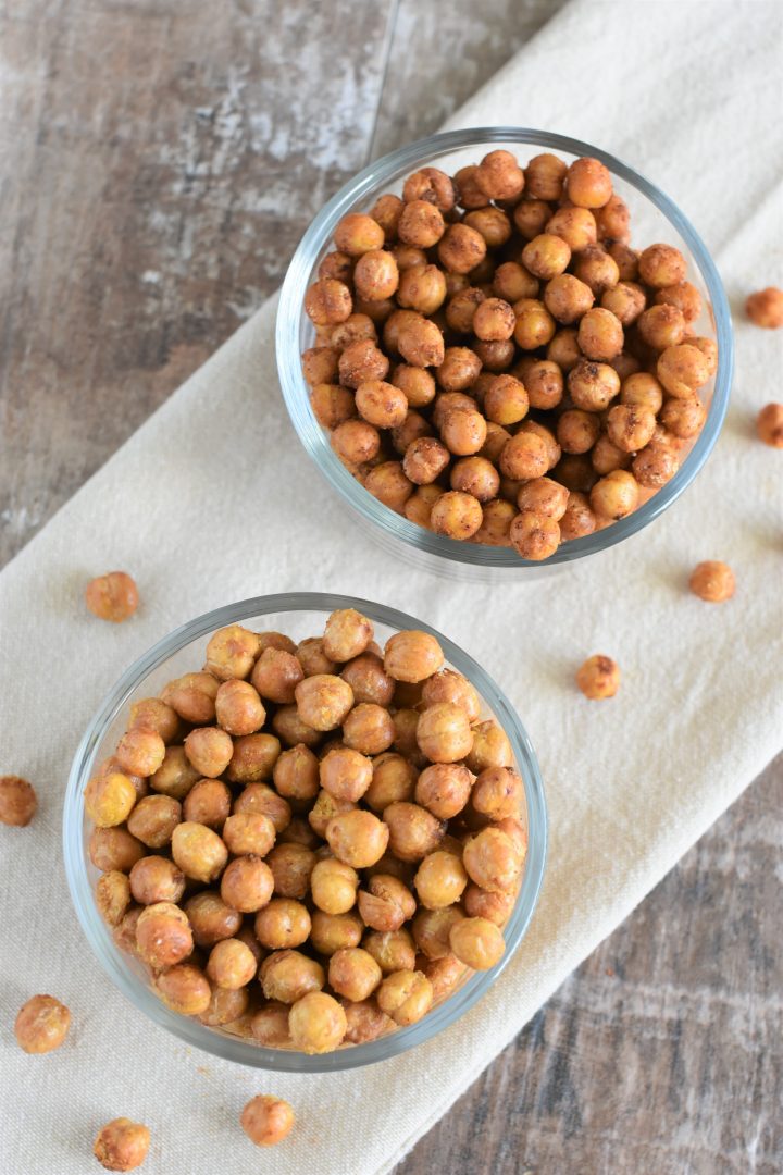 Bowl of cheesy air fryer chickpeas in front of bowl of taco fiesta air fryer chickpeas on kitchen towel with some chickpeas on the towel