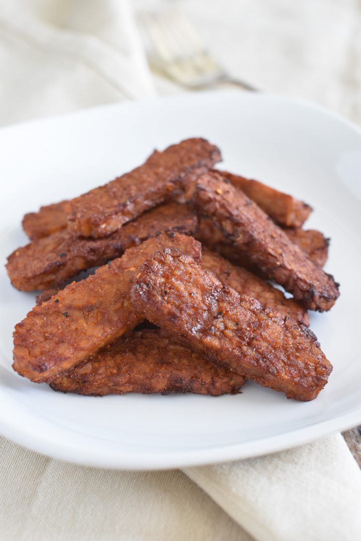 Tempeh bacon on white plate on top of kitchen napkins