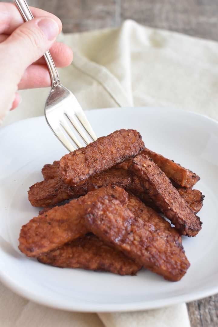 Picking up a piece of the bacon from the white plate with a fork