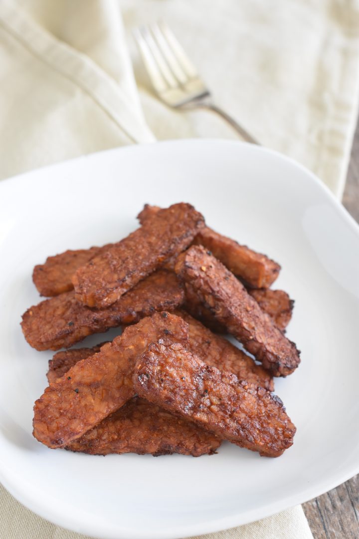 cooked tempeh on a white plate on a kitchen napkin with fork in the background