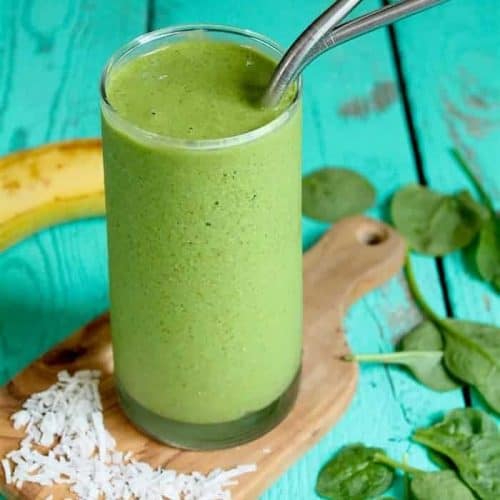 tropical green smoothie in a glass with two straws.