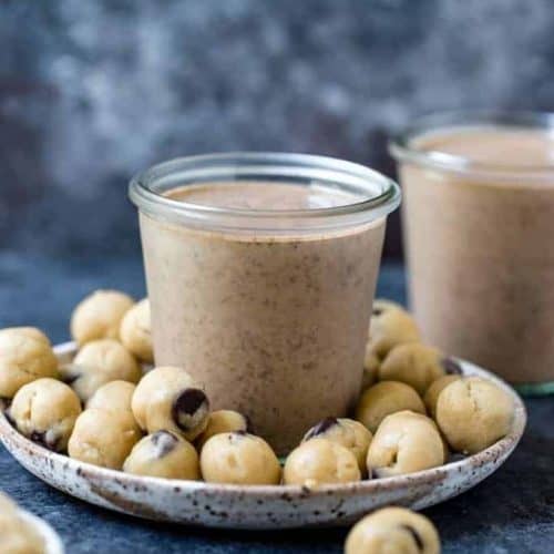 cookie dough smoothie in a glass on a plate with cookie dough balls.