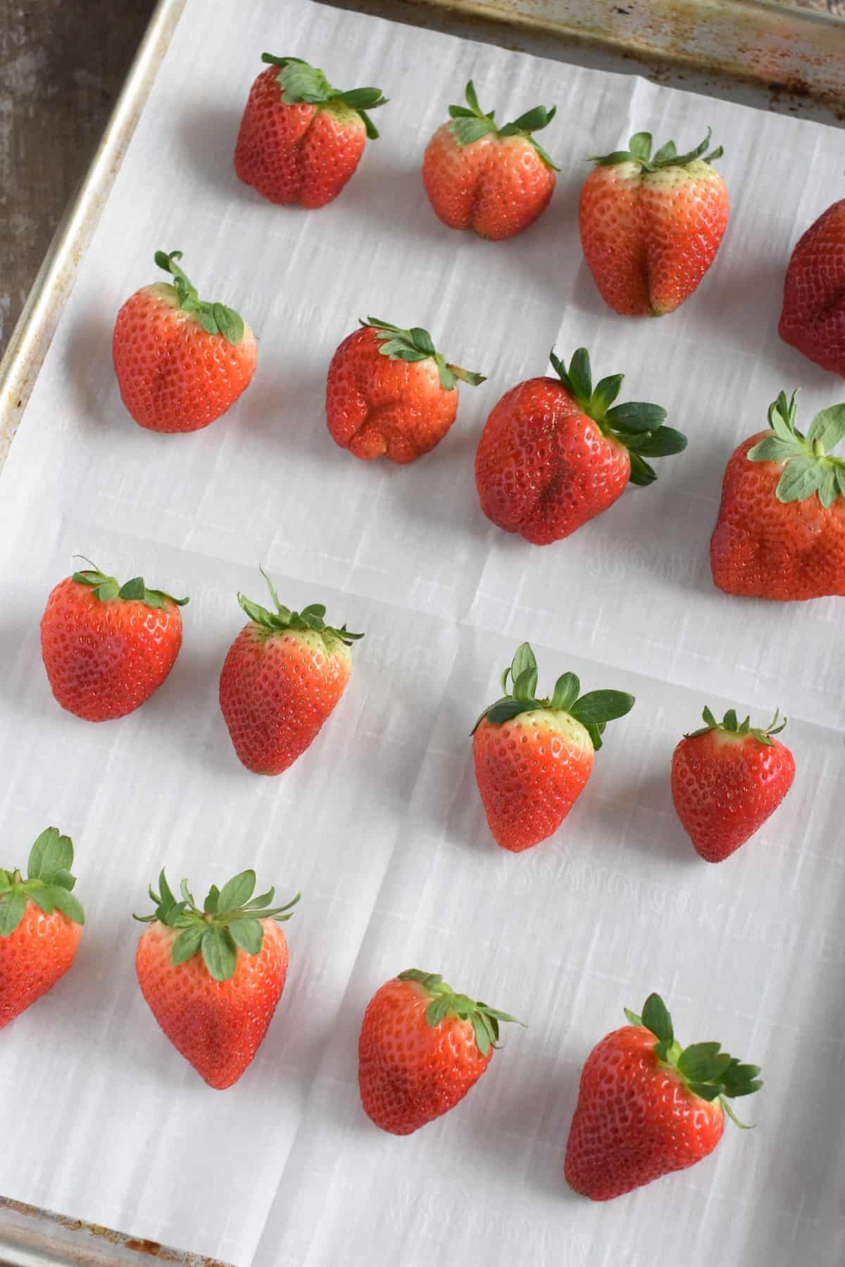 strawberries on a parchment-lined baking sheet ready to be dipped