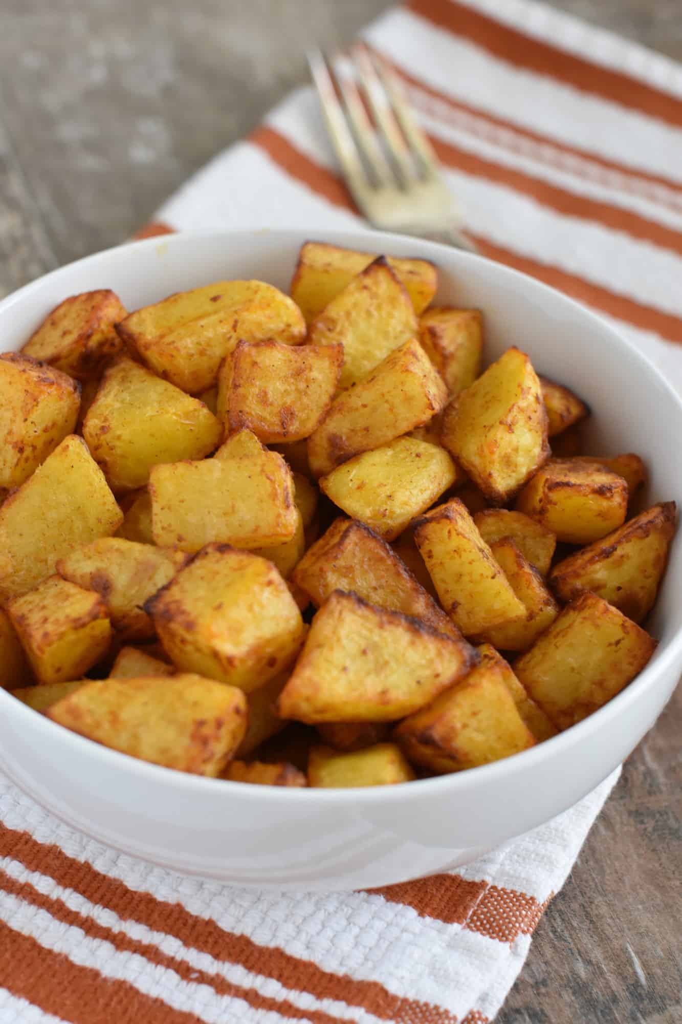 breakfast potatoes in white serving bowl with fork behind it