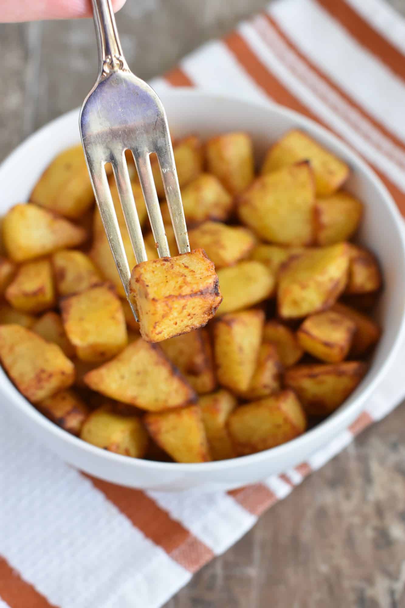 holding up one of the potatoes with a fork over the bowl of the rest of them