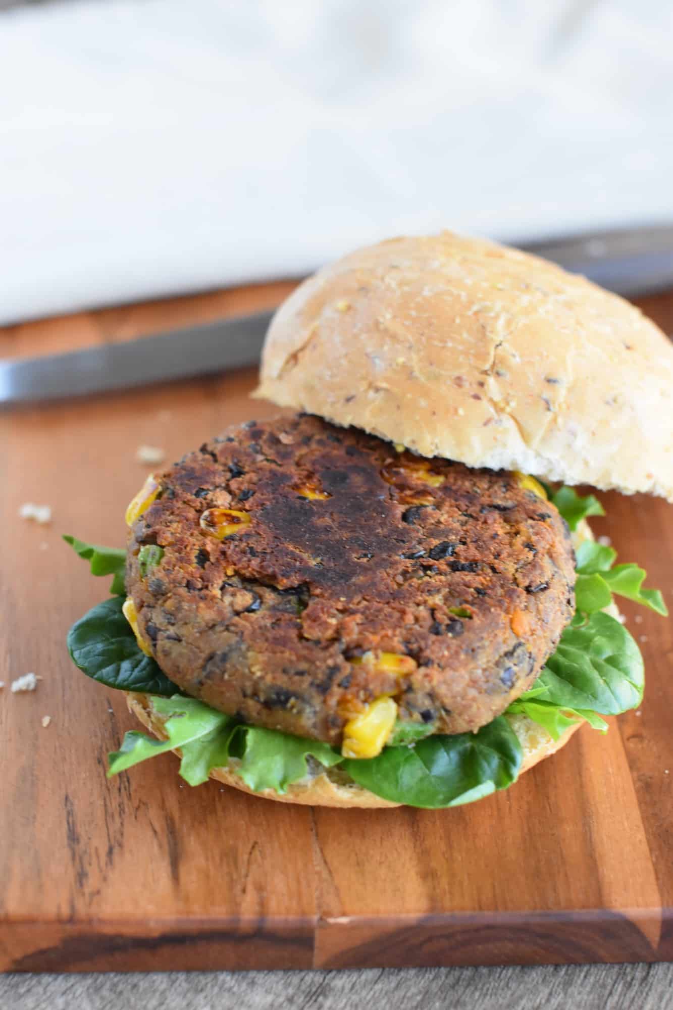 burger on a bun with lettuce on wooden board waiting for toppings