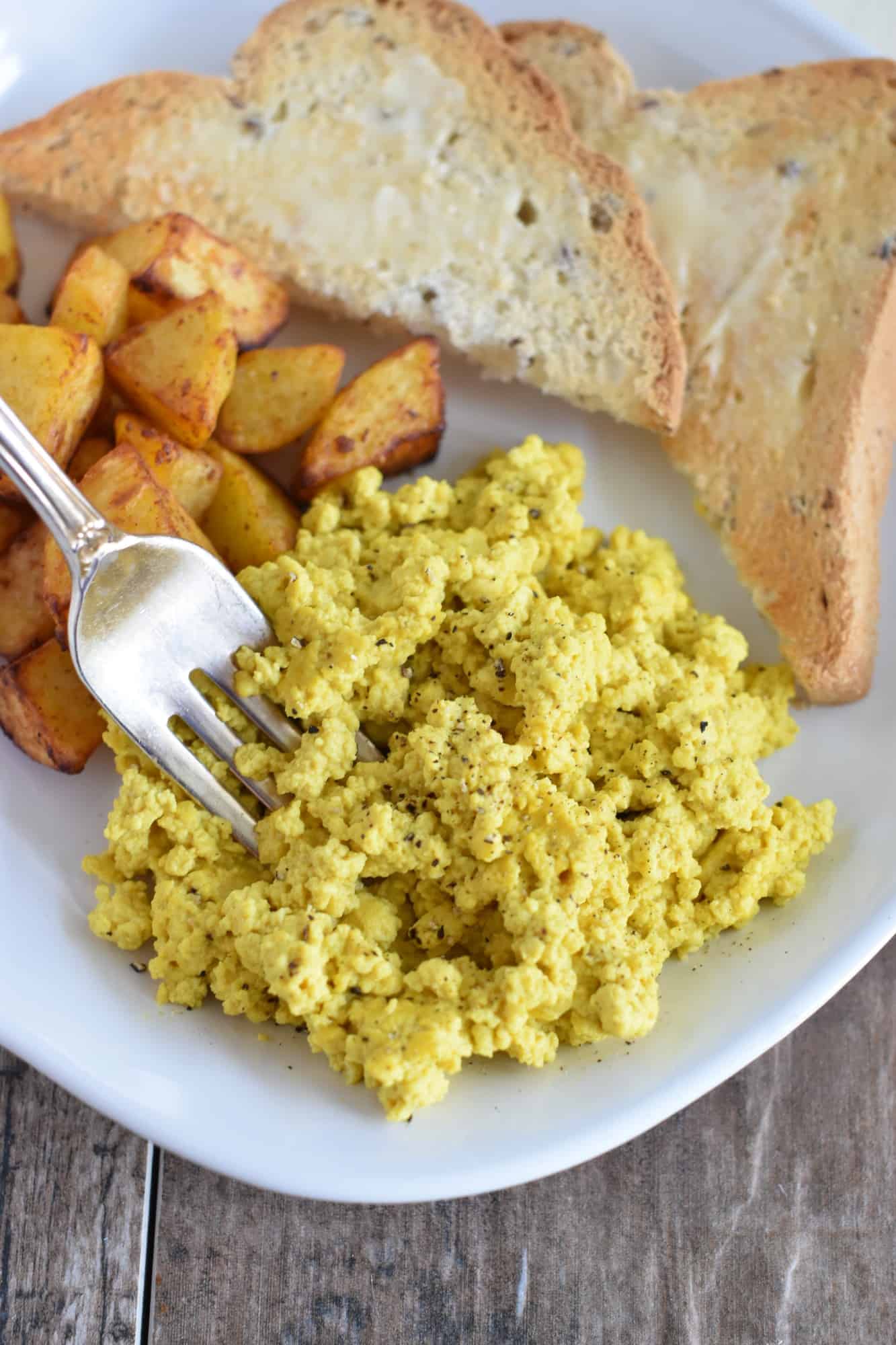 taking some vegan tofu scramble with a fork with potatoes and toast behind it on the same plate