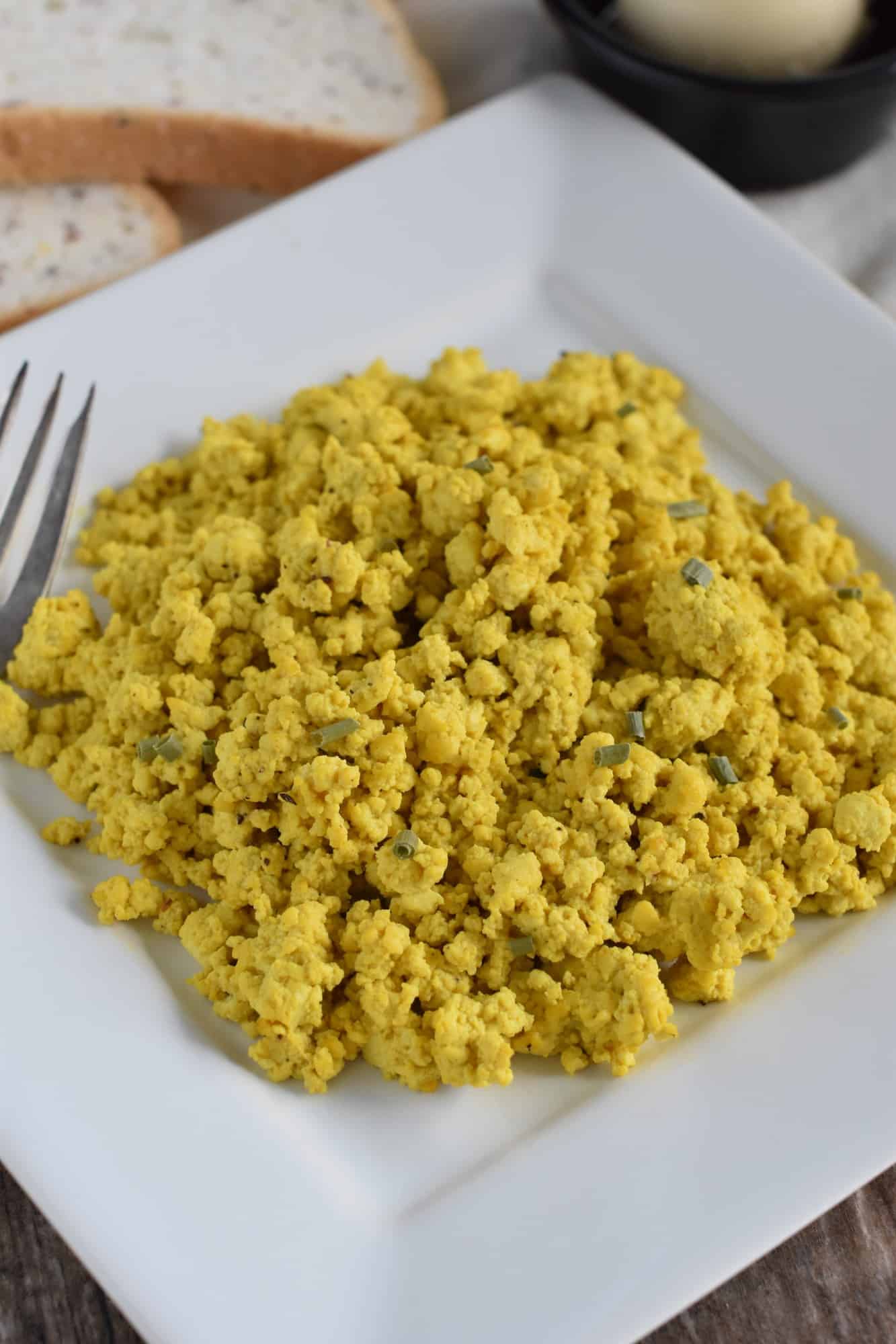 vegan scramble on white plate with fork next to it and some bread and vegan butter in background