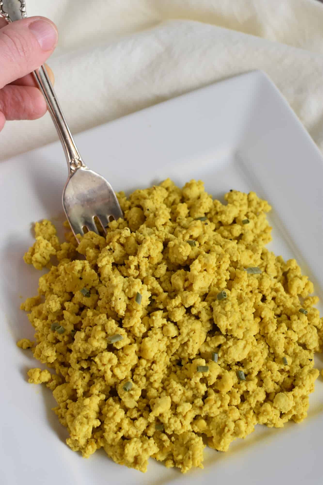 hand holding fork in breakfast scramble on white plate