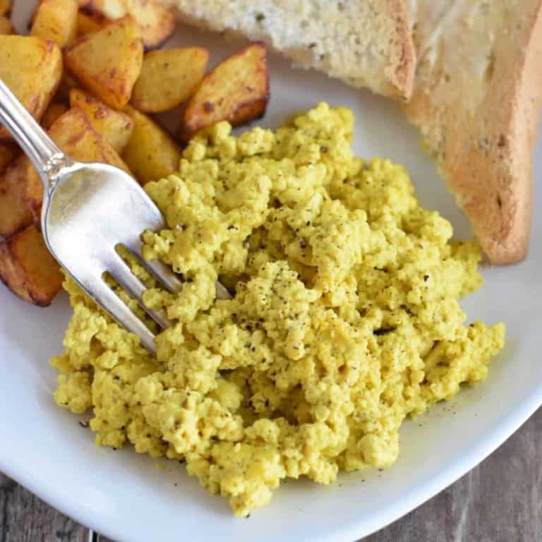 tofu eggs on a plate with a fork in it and some potatoes and toast behind it