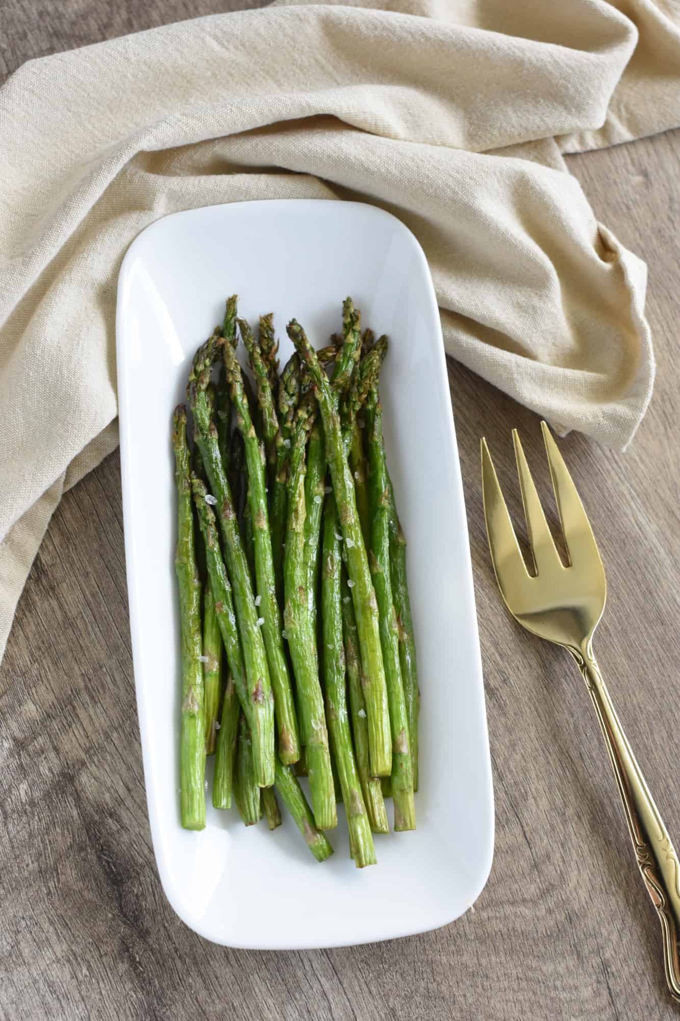 air fryer asparagus on white serving dish with fork next to it