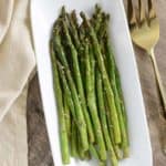 overhead of asparagus on white serving dish with large serving fork next to it