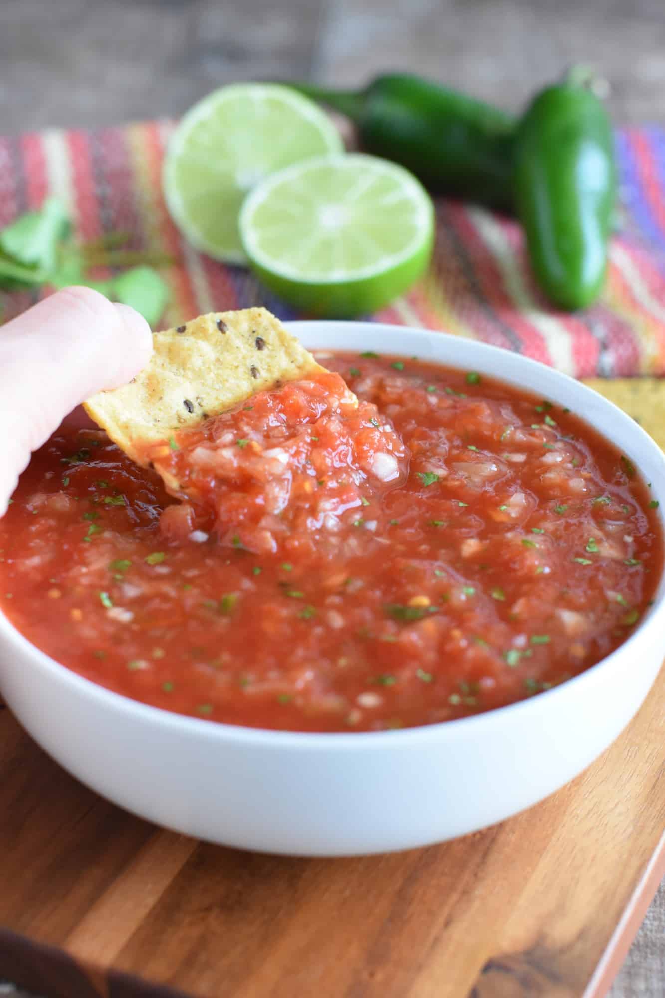 Dipping a chip into the salsa with cilantro, lime and jalapeno in the background