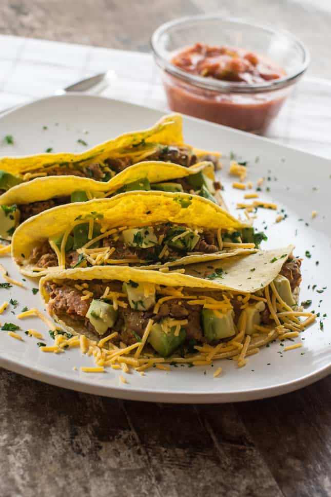 Tacos on a white plate with vegan cheese shreds and salsa in the background