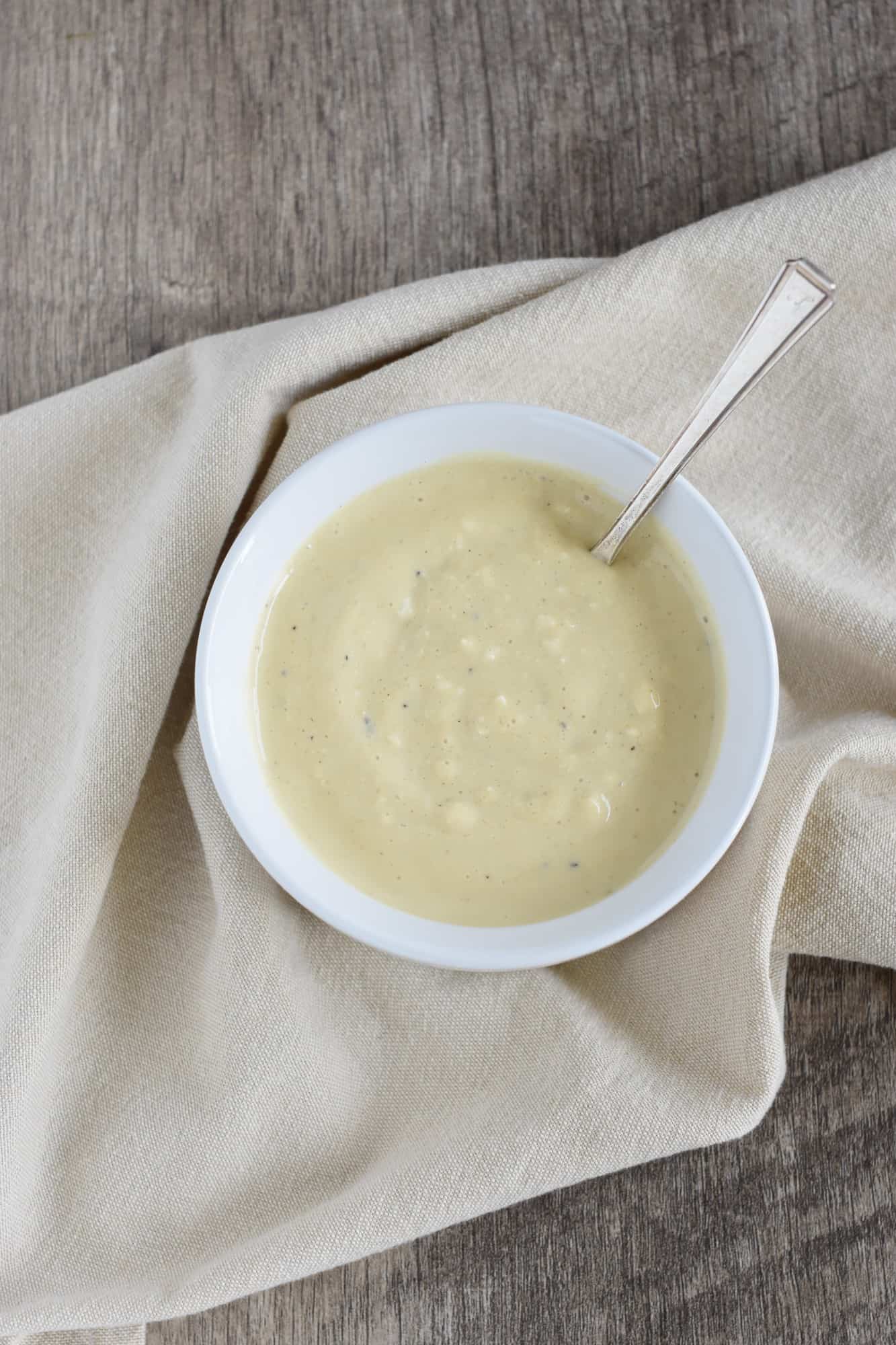 overhead of dressing in white serving bowl with spoon in it