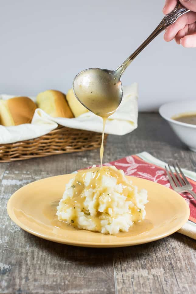 using a ladle to pour gravy onto mashed potatoes on a plate