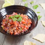 homemade salsa in a black bowl with some tortilla chips around it