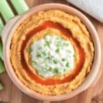 overhead of hummus in a serving bowl on a wooden board with some celery sticks