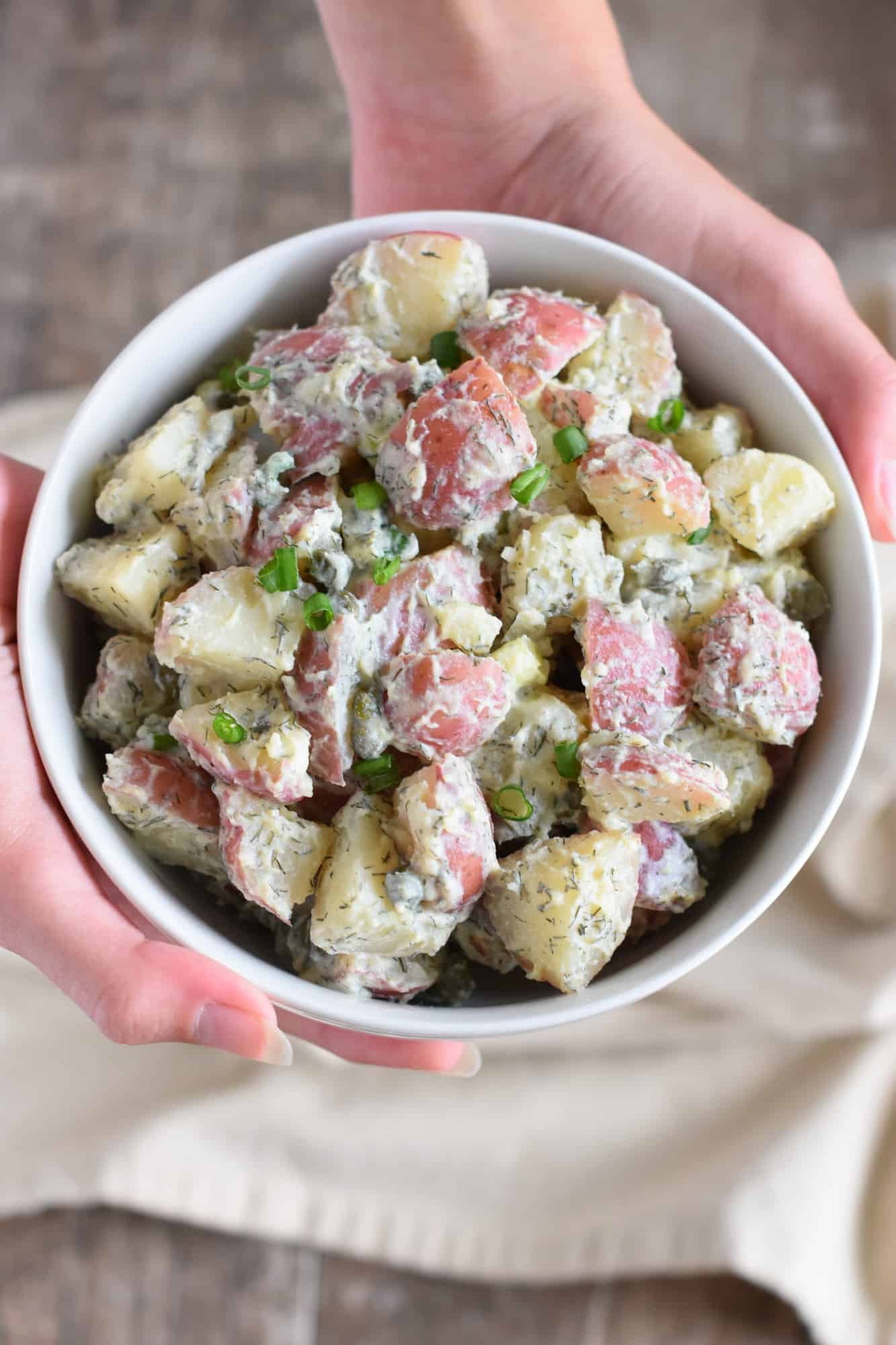 overview of hands holding up potato salad in a white bowl