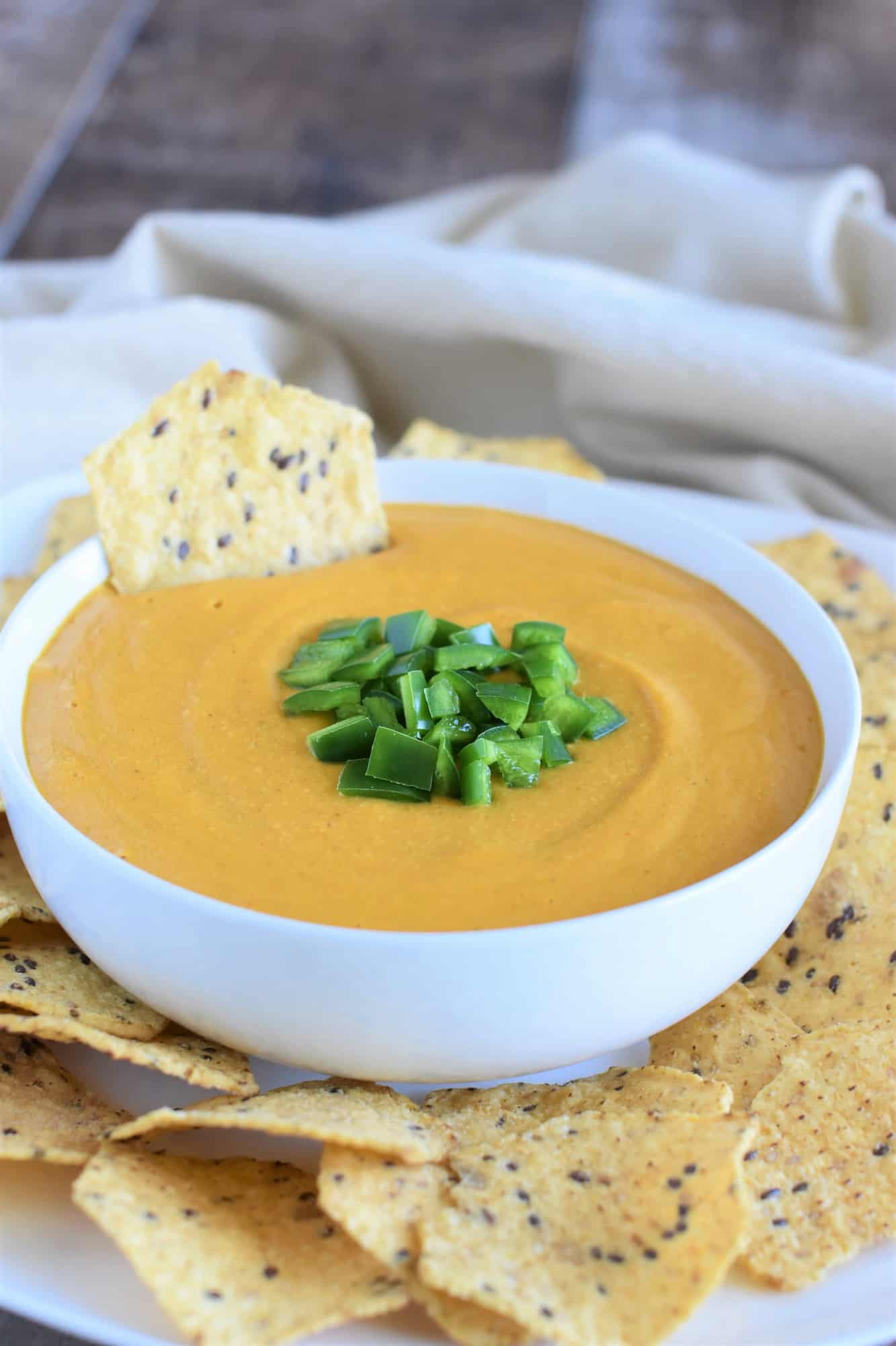 tortilla chip sitting in bowl of sauce on a white platter with more chips