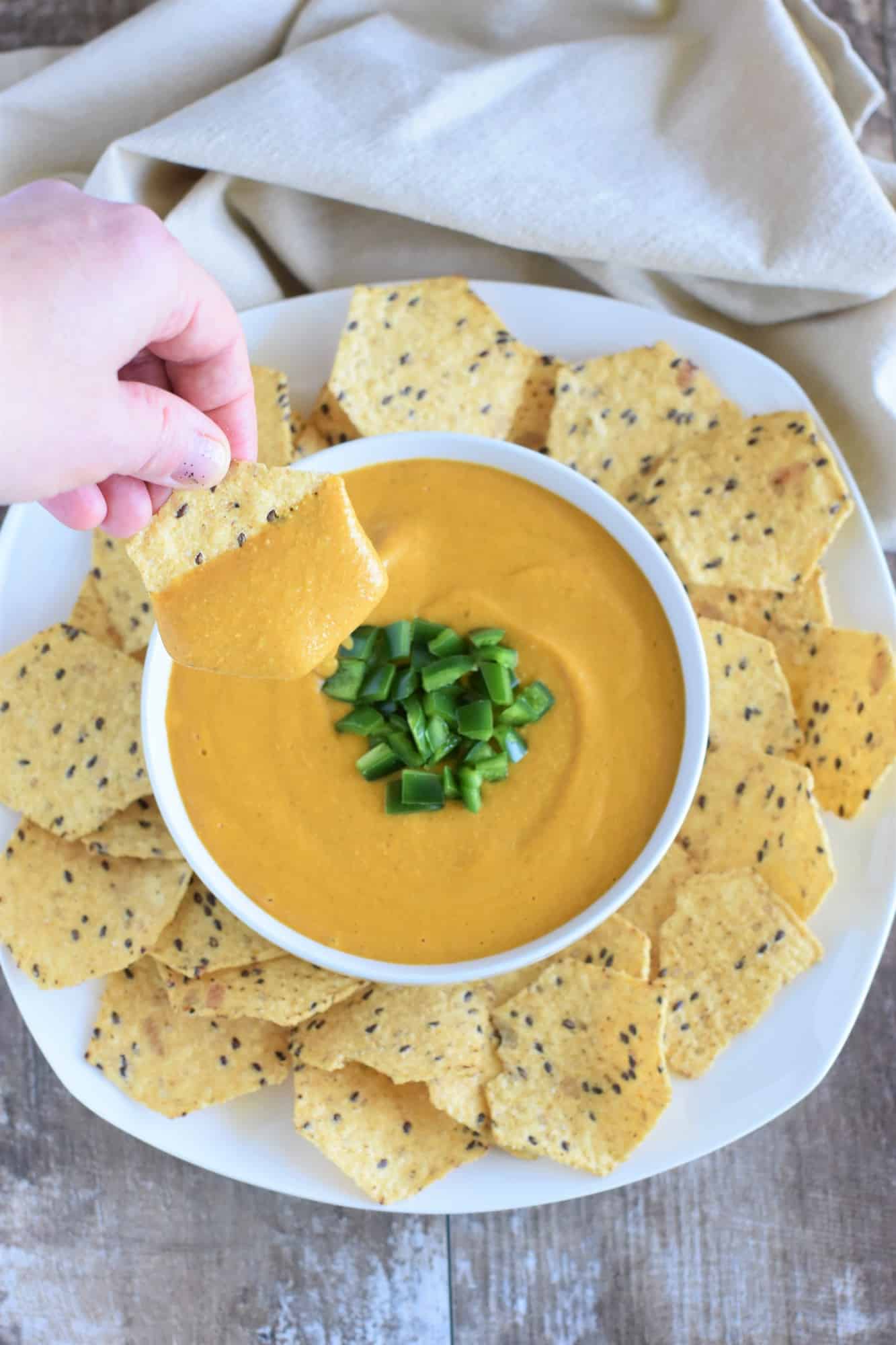 holding a chip dipped in the sauce over the bowl of sauce with chips on a white plate