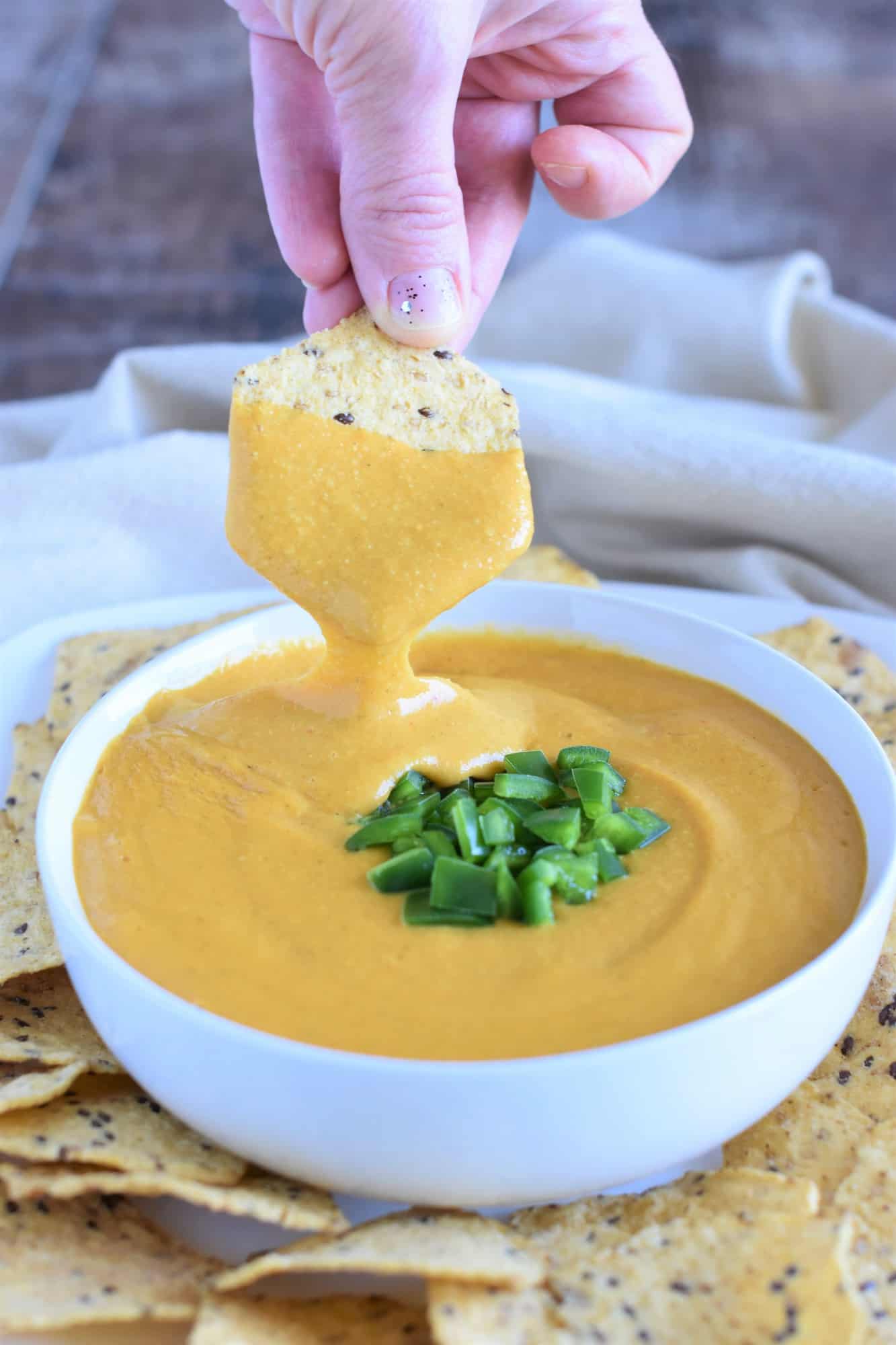 dipping a tortilla chip into the sauce in a white bowl