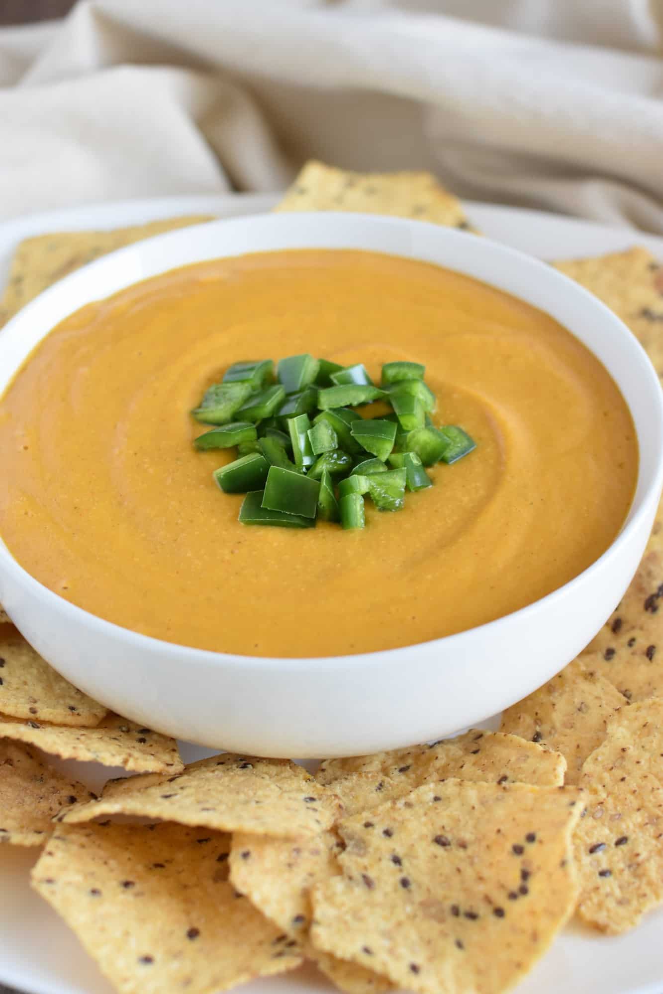 nacho sauce in a white bowl with chips around it