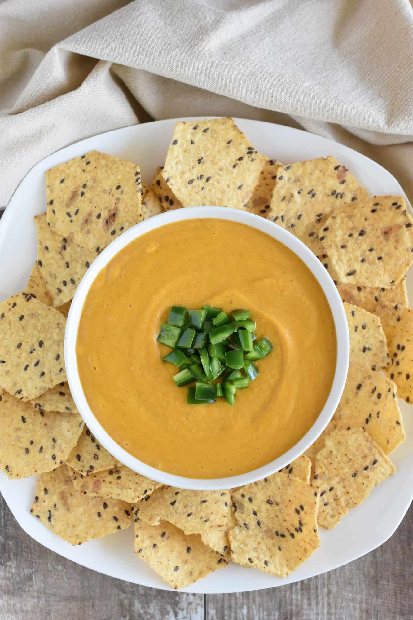 vegan nacho cheese sauce in a white serving bowl with tortilla chips around it on a white platter