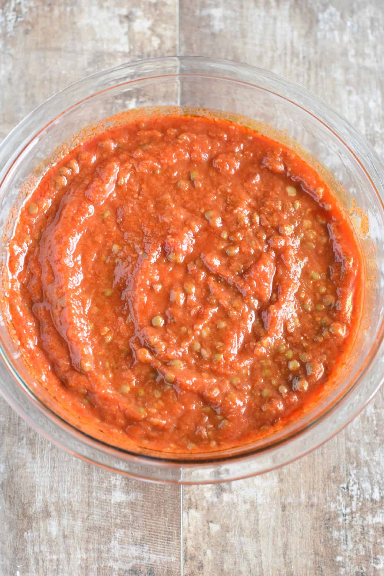 lentils stirred into the pasta sauce in the mixing bowl