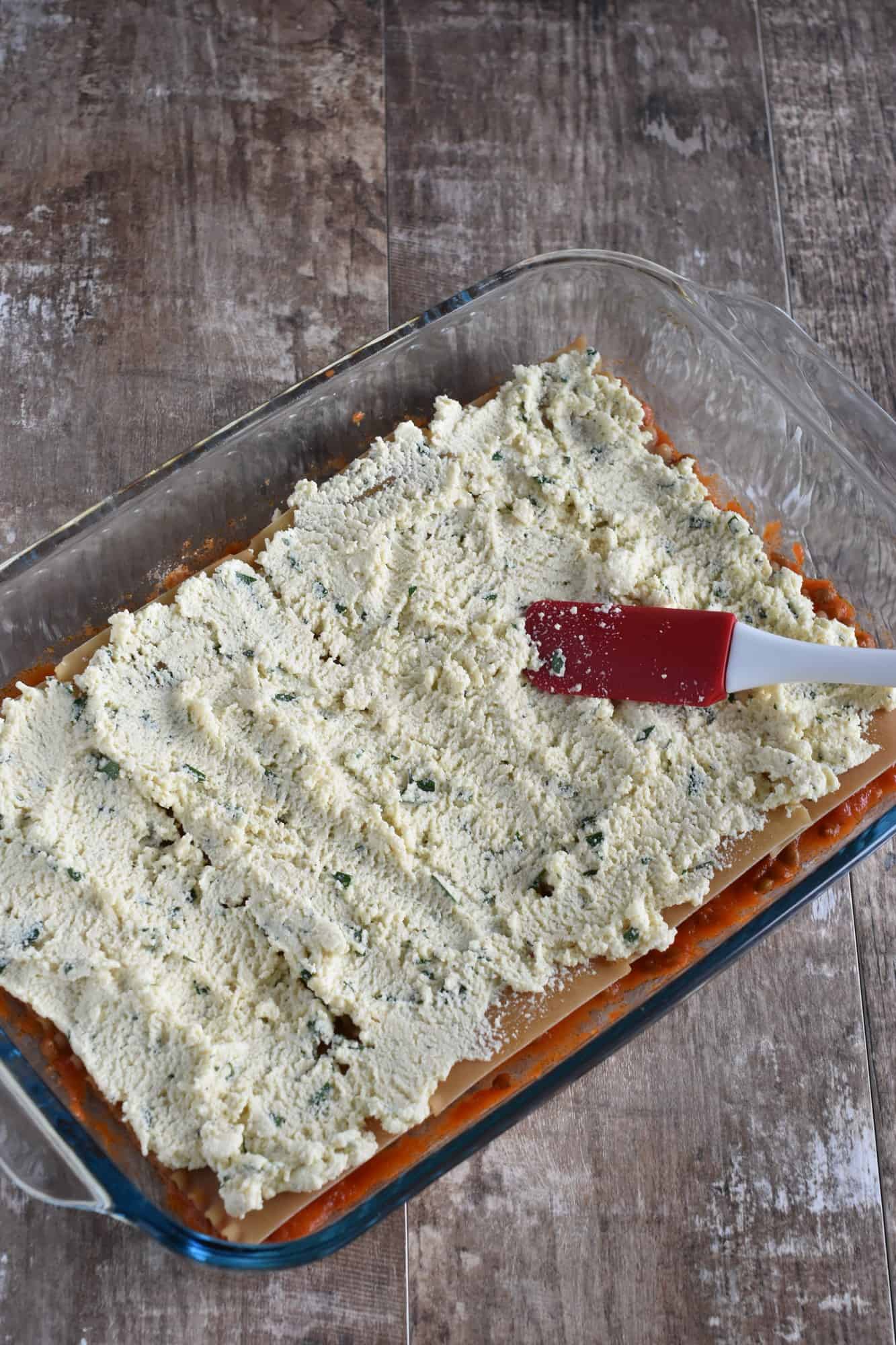 spreading the ricotta across the noodles with a silicone spatula