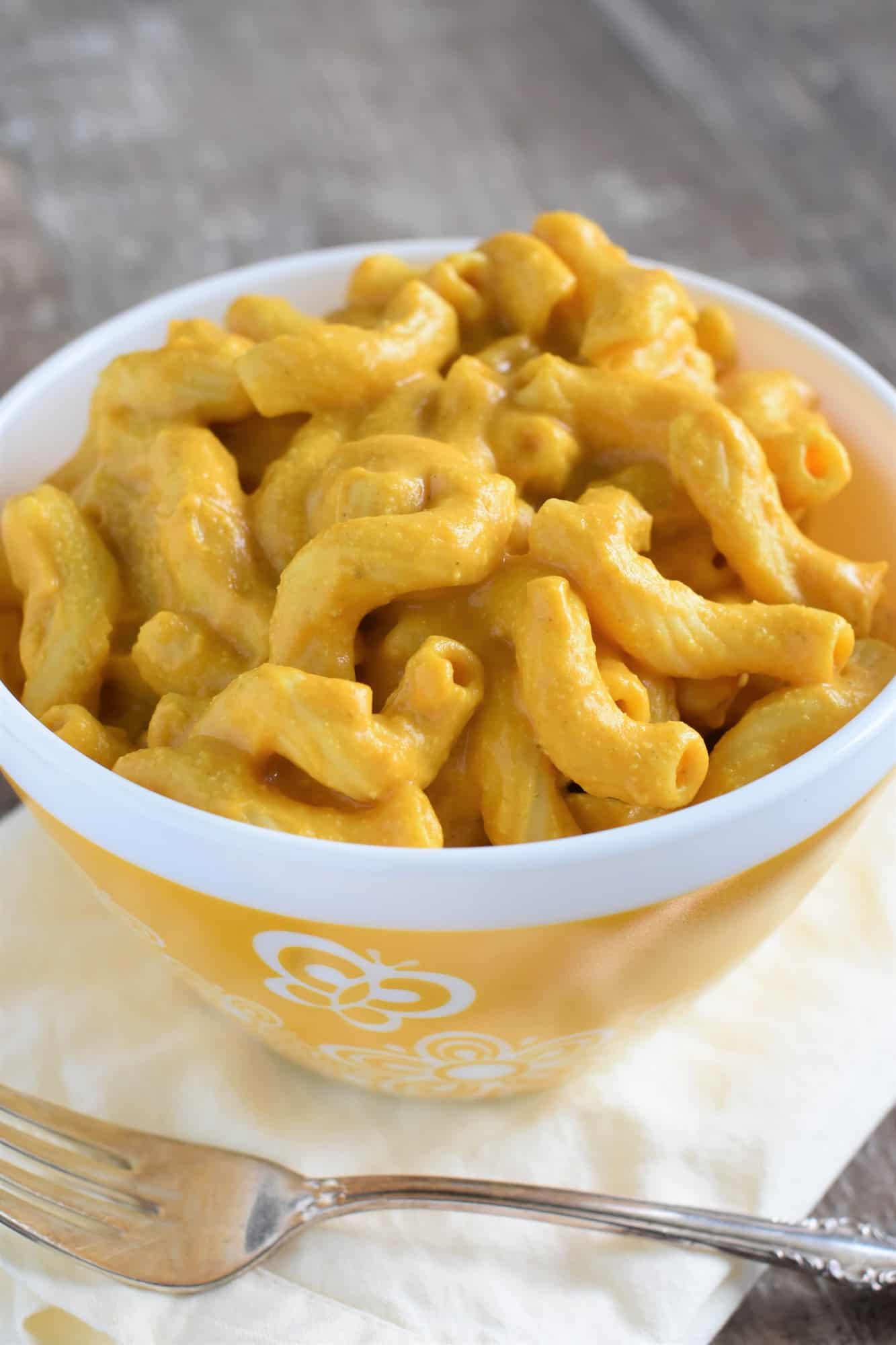 front view of serving of mac and cheese in a decorated yellow bowl with a fork in front of it