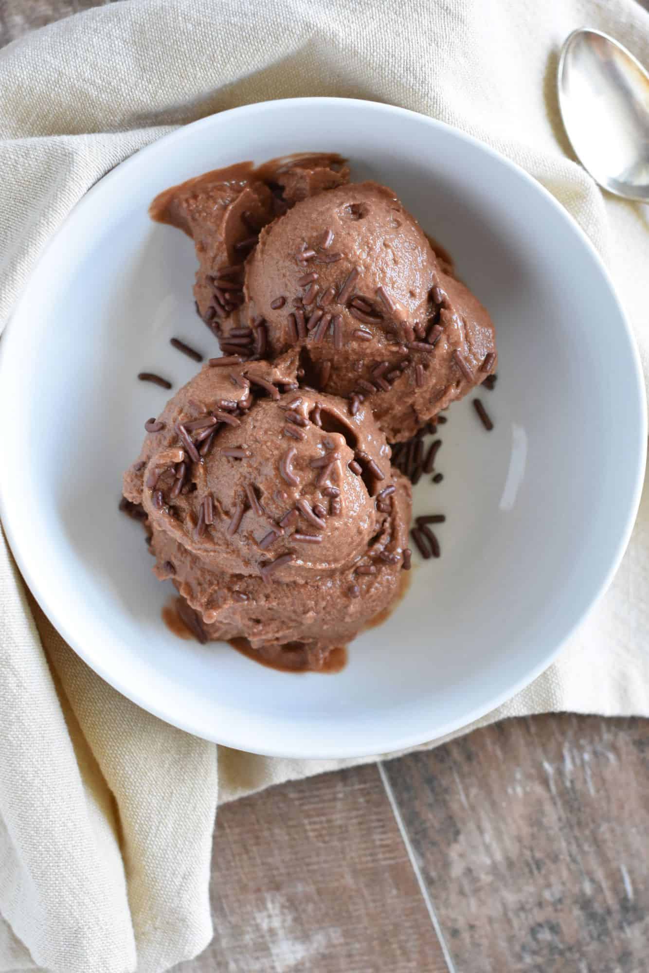 overhead of nice cream in a white bowl topped with sprinkles on a kitchen napkin with a spoon next to the bowl