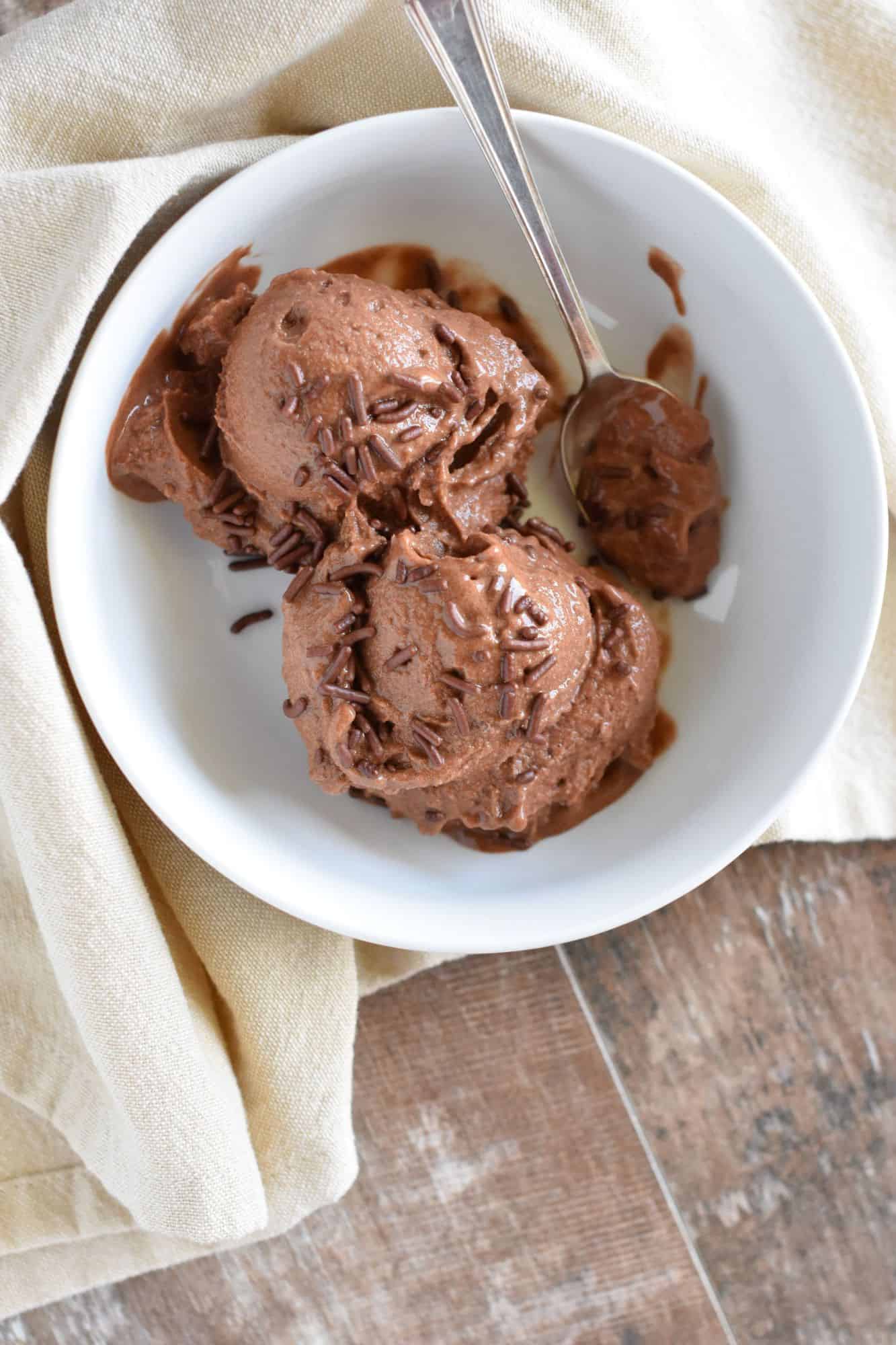 overhead of chocolate nice cream in a white bowl with a spoon and some sprinkles