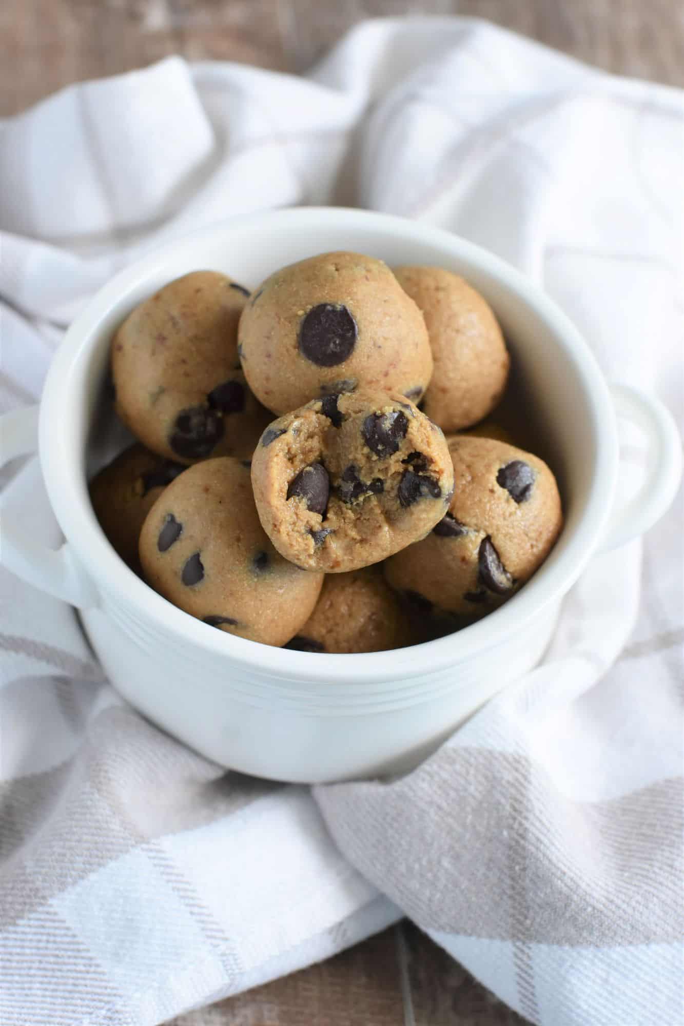 dough balls in a small white bowl with a bite taken out of one of them to show the inside