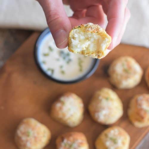 closeup of open mashed potato ball being held by a hand over more on a wooden board