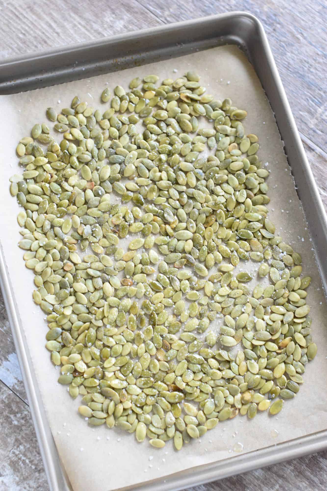 raw pepitas with avocado oil spray and salt on the baking sheet