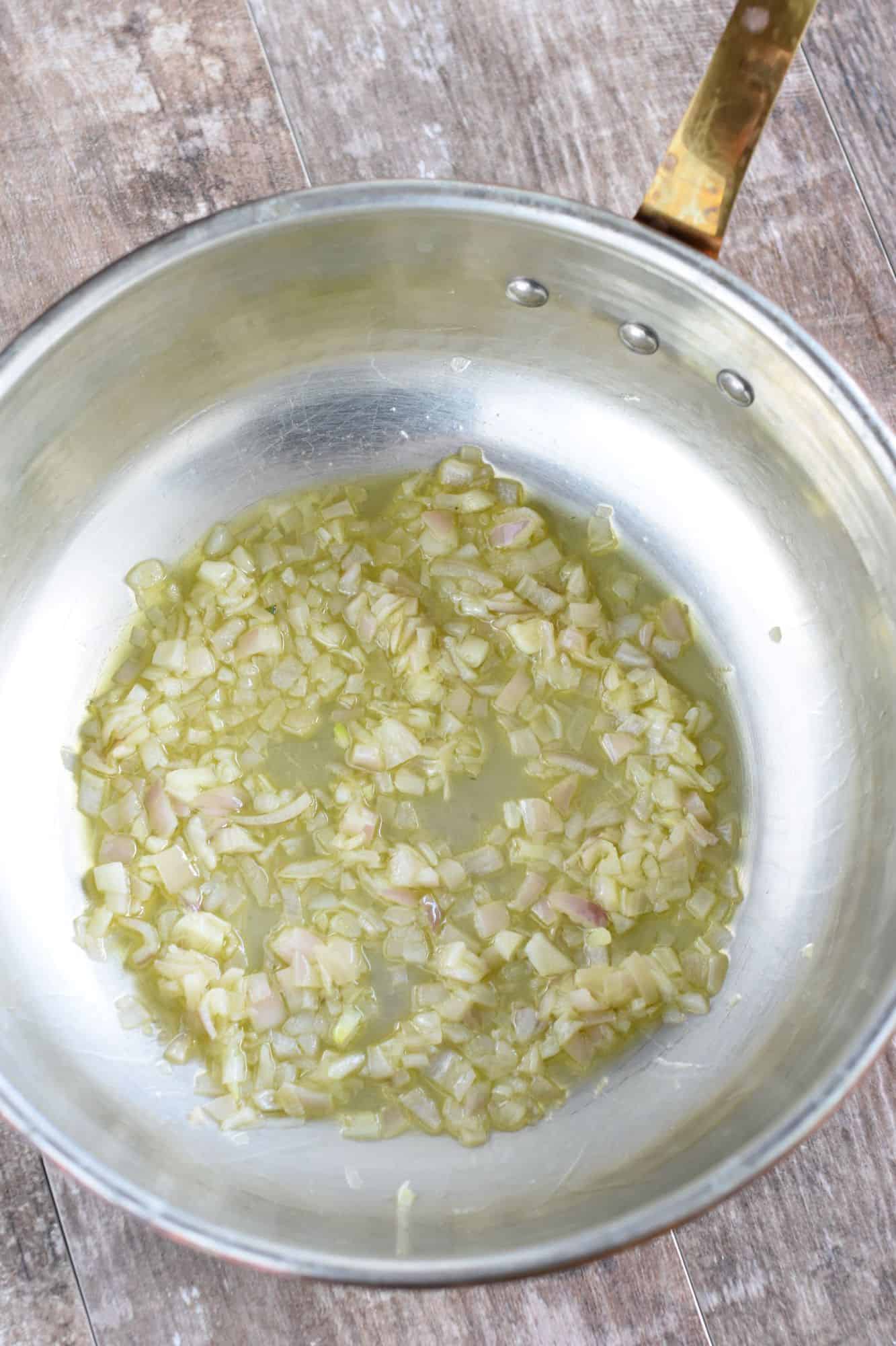 Chopped shallots cooking in olive oil in a risotto pan