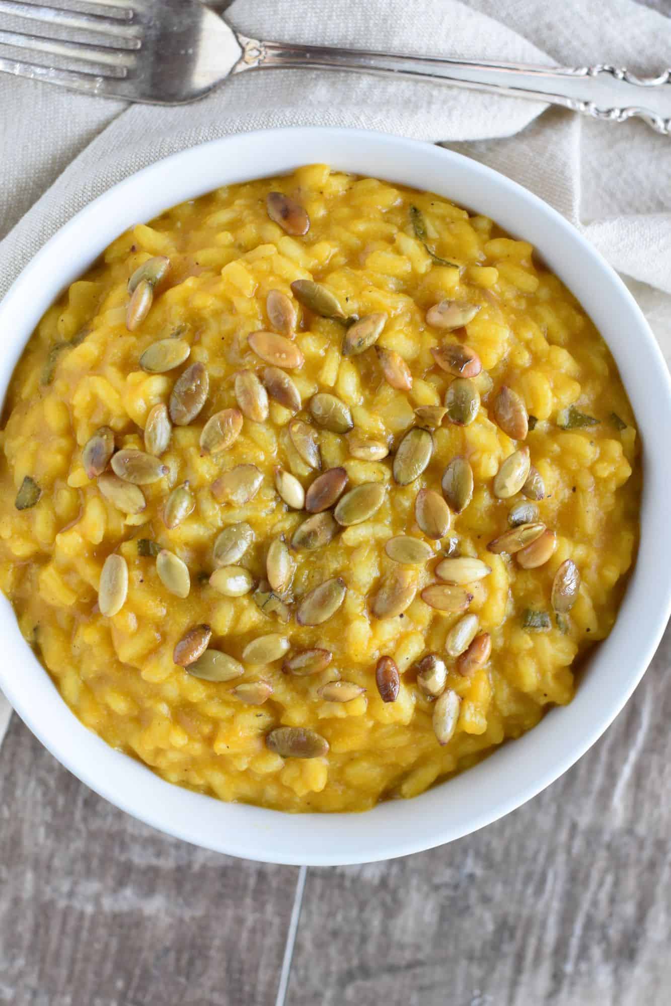 overhead of risotto in a white bowl with roasted pepitas spread out on top