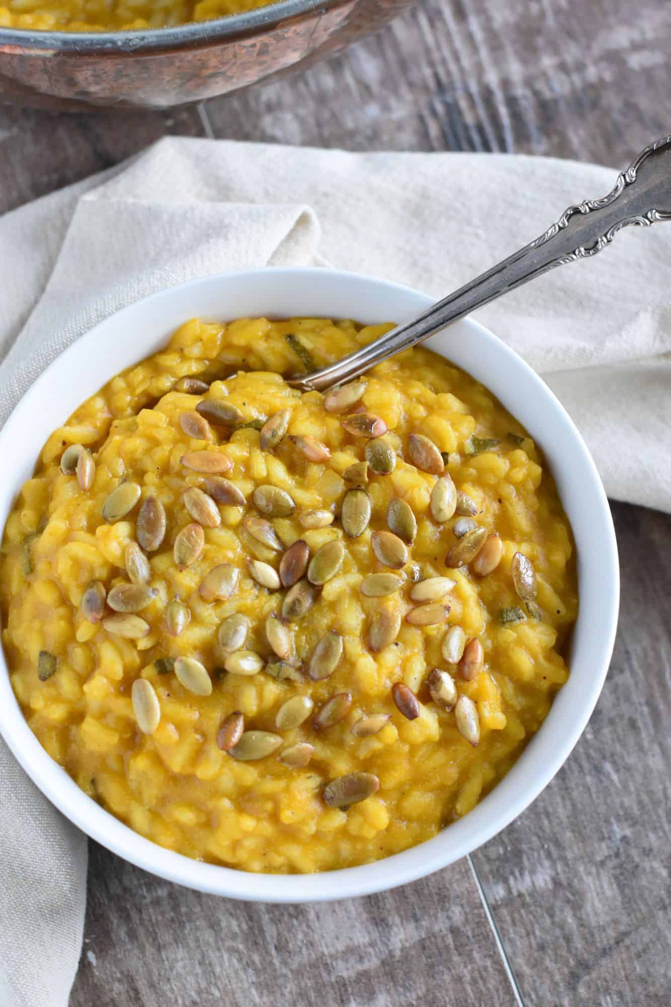 overhead of risotto in a white bowl with roasted pepitas spread around on top and a fork in it