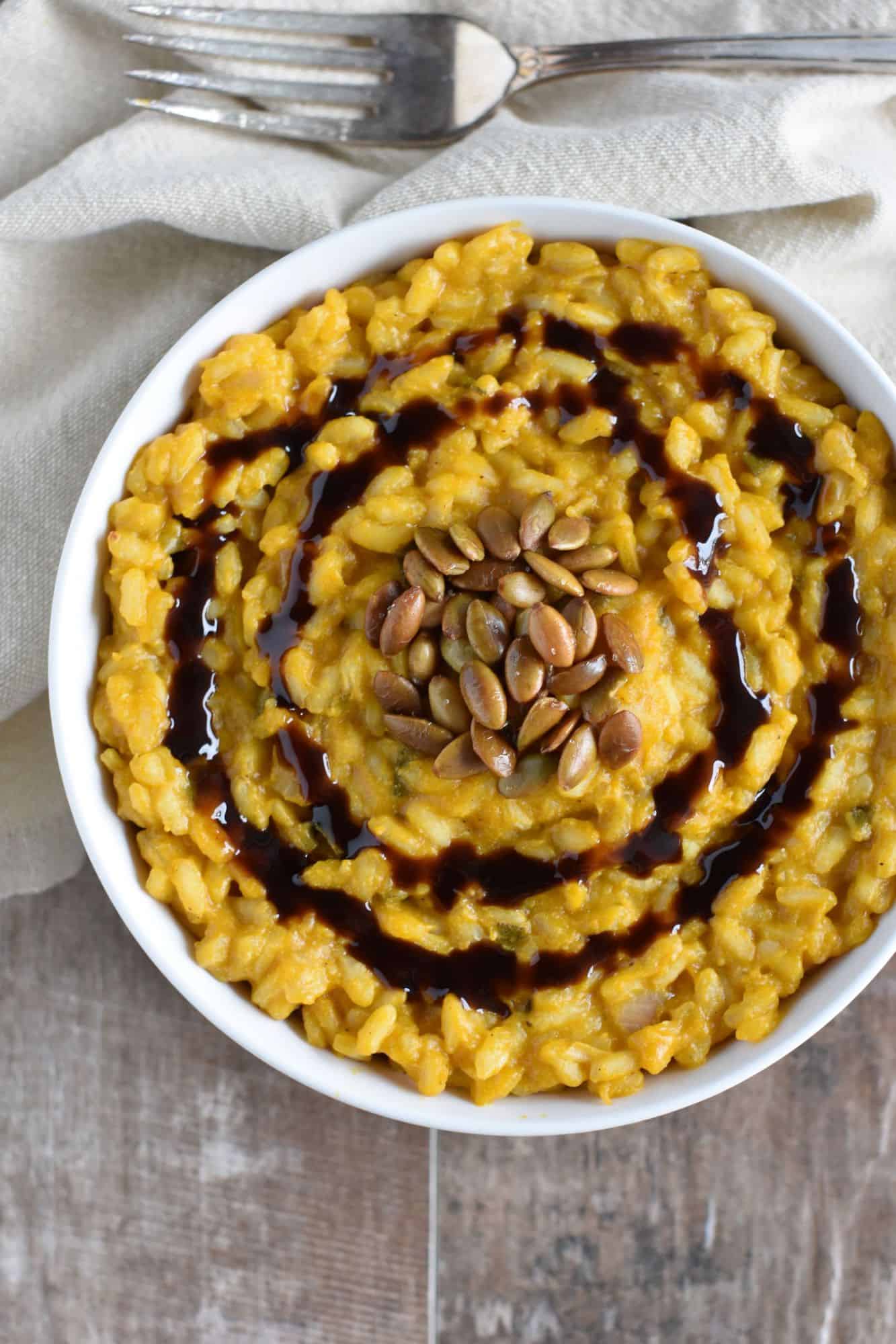 overhead of vegan pumpkin risotto in a white bowl with roasted pepitas and balsamic glaze