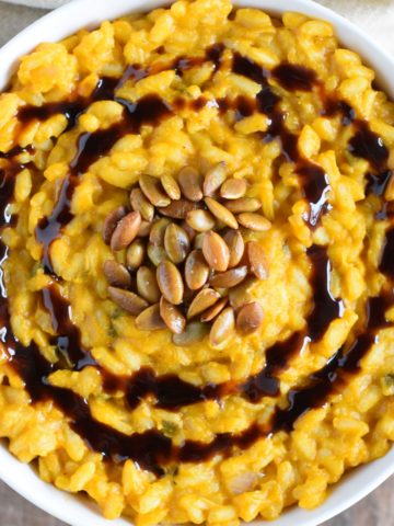 overhead of risotto in a white bowl garnished with roasted pepitas and balsamic glaze