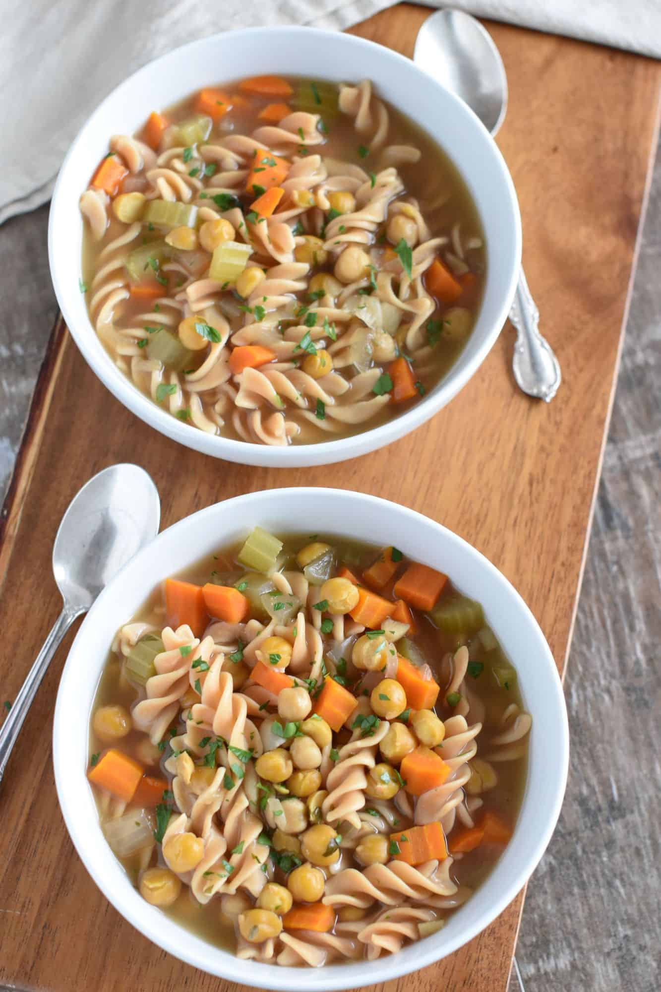 two bowls of soup on a wooden board with spoons next to them