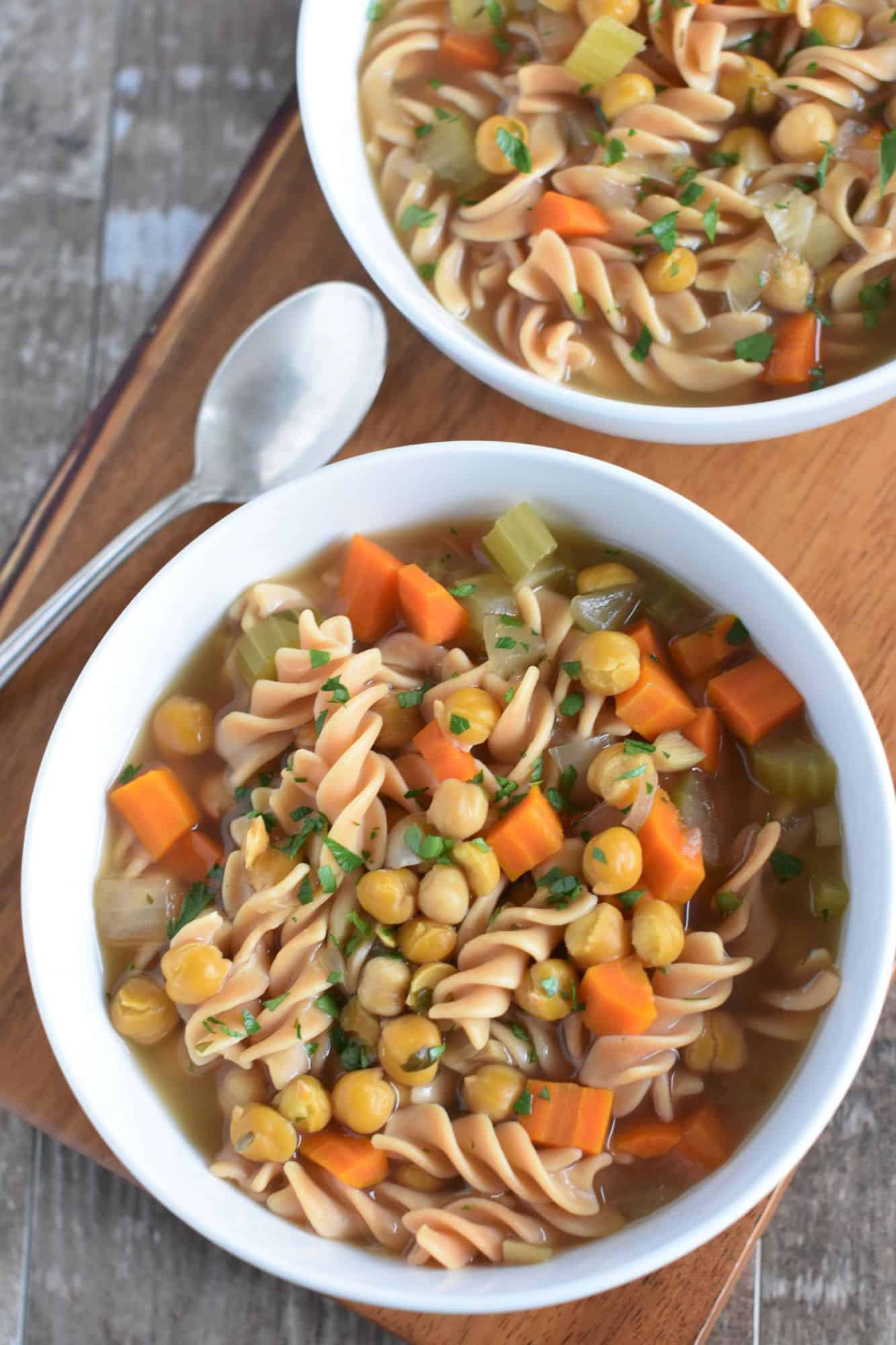 soup in a white bowl on a wooden board with a spoon next to it with half of another bowl of soup showing behind it