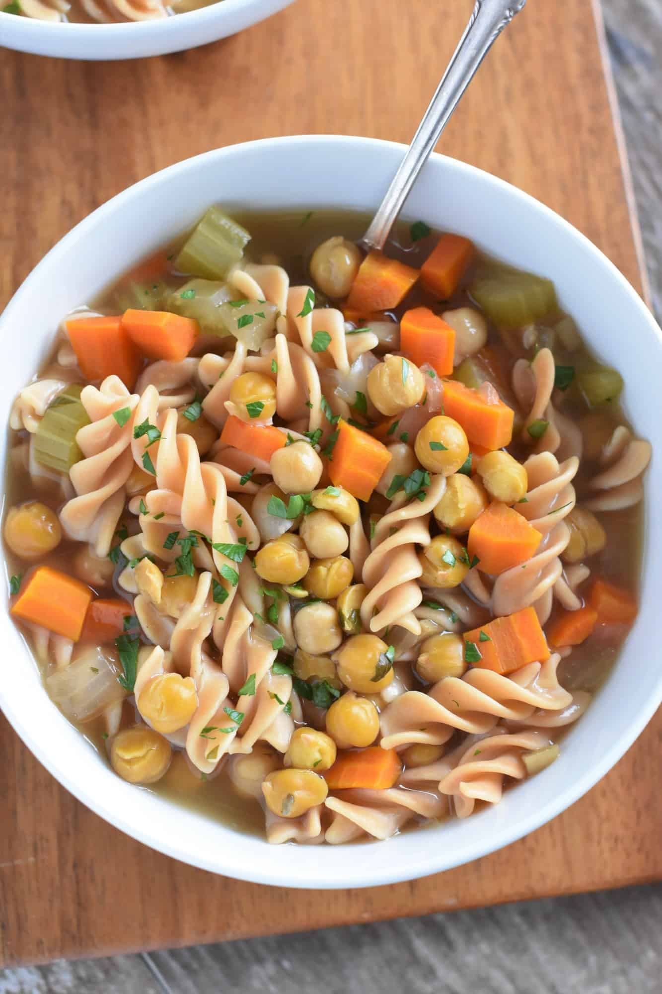 closeup overhead of chickpea noodle soup in a white bowl with a spoon in it