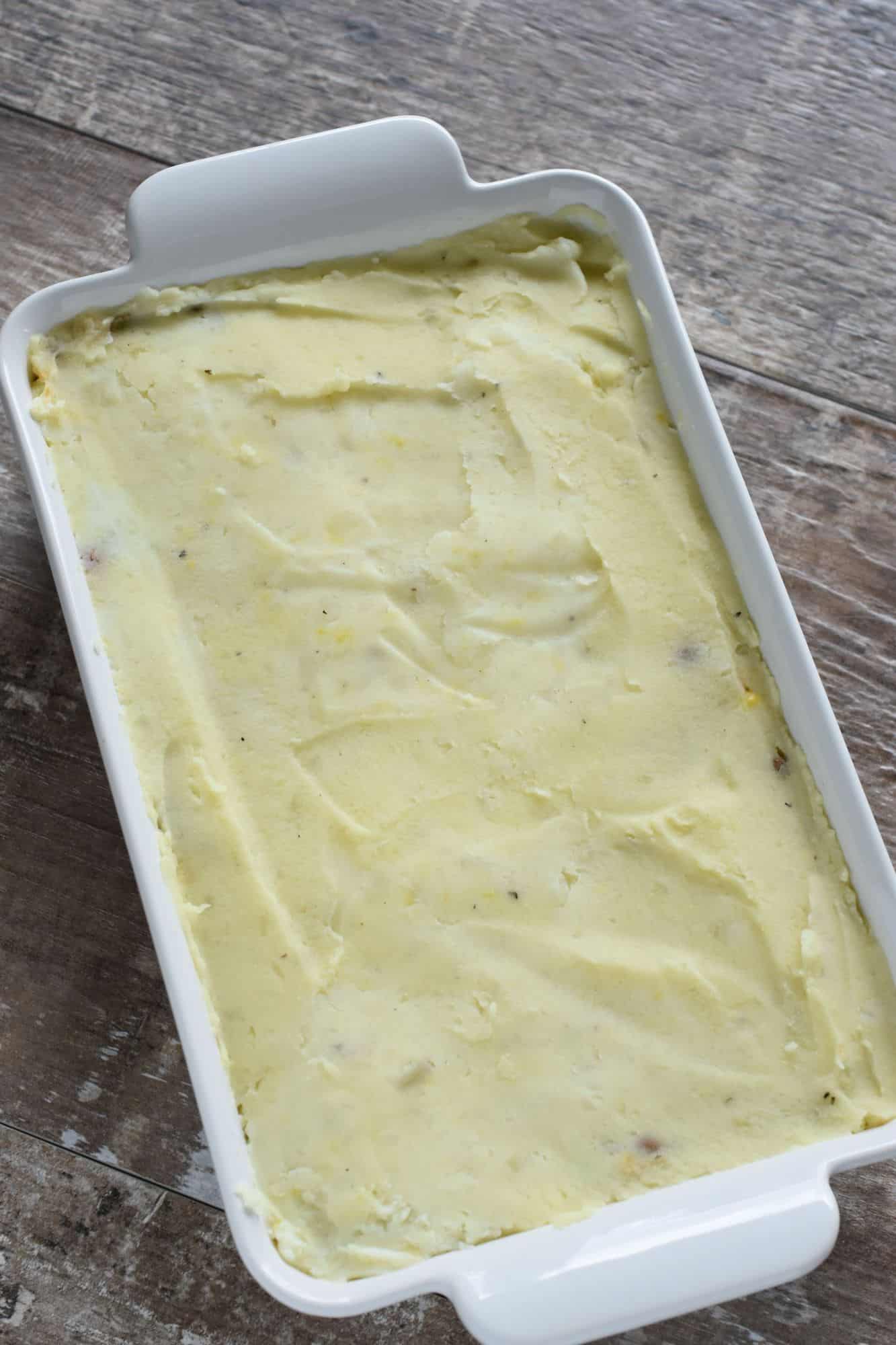 mashed potatoes spread on top of the filling in the casserole dish