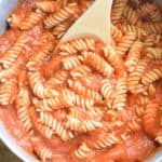 stirring pasta and pumpkin tomato sauce together in a pot with a wooden spoon