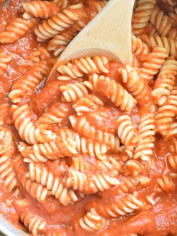 stirring pasta and pumpkin tomato sauce together in a pot with a wooden spoon