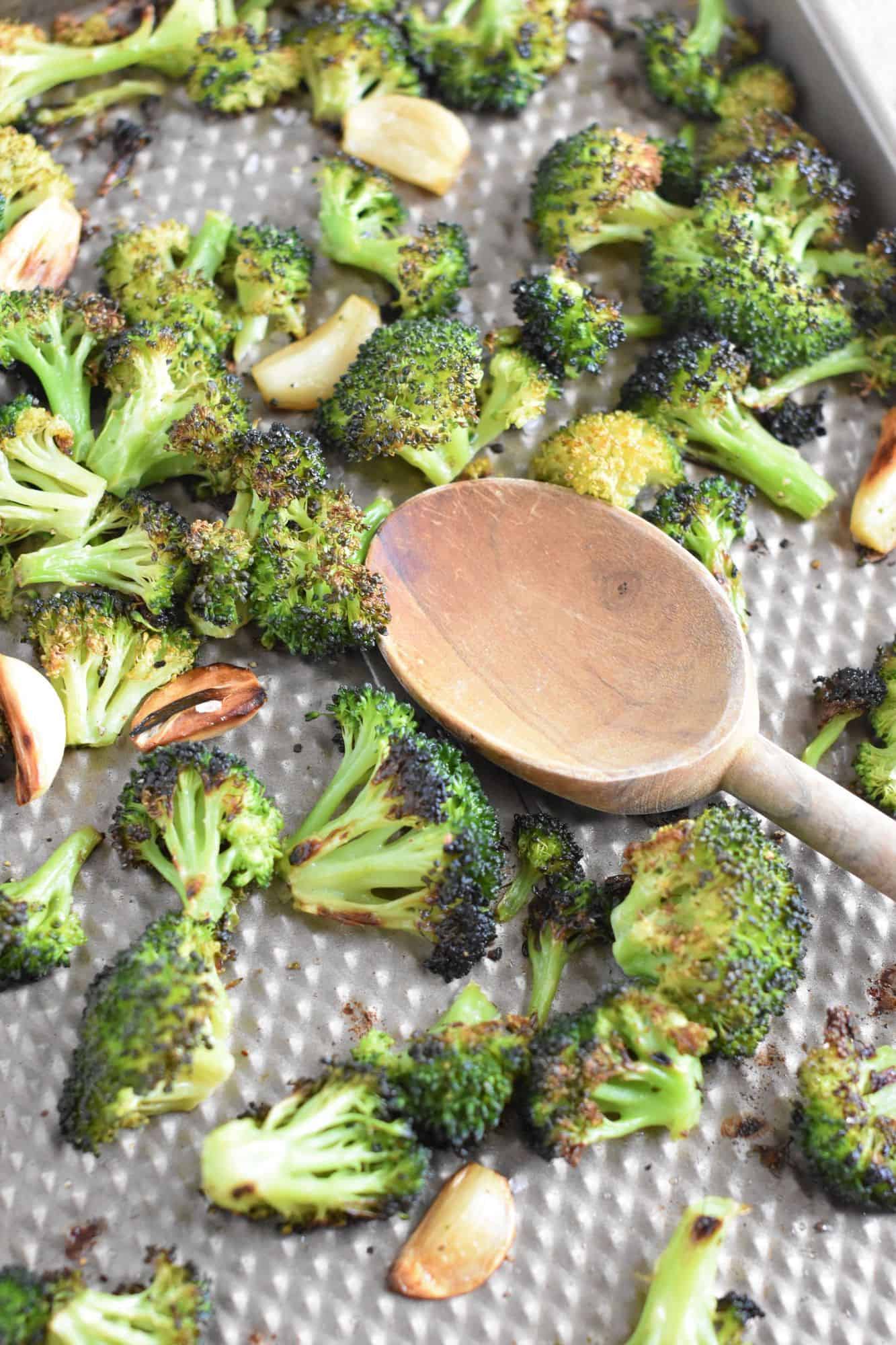 broccoli and garlic on baking sheet with wooden spoon after being cooked